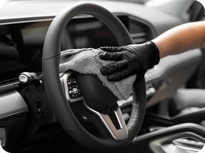 Car interior detailing process cleaning steering wheel with microfiber cloth and protective gloves
