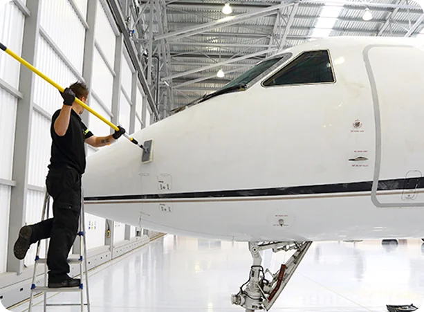 Jet cleaning and detailing process inside modern aircraft hangar with technician on ladder